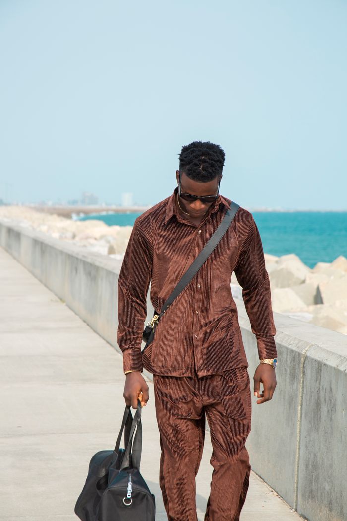 Man in brown suit walking along a seaside promenade carrying a leather bag.