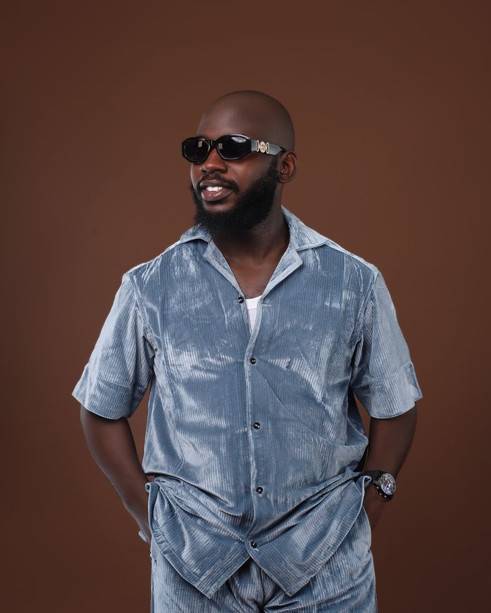 Portrait of a fashionable man wearing sunglasses and a gray velvet shirt, hands in pockets.