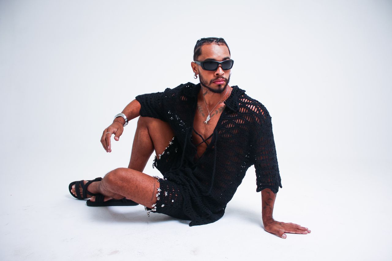 gallery-01 Man in trendy black crochet outfit and sunglasses in studio setting.