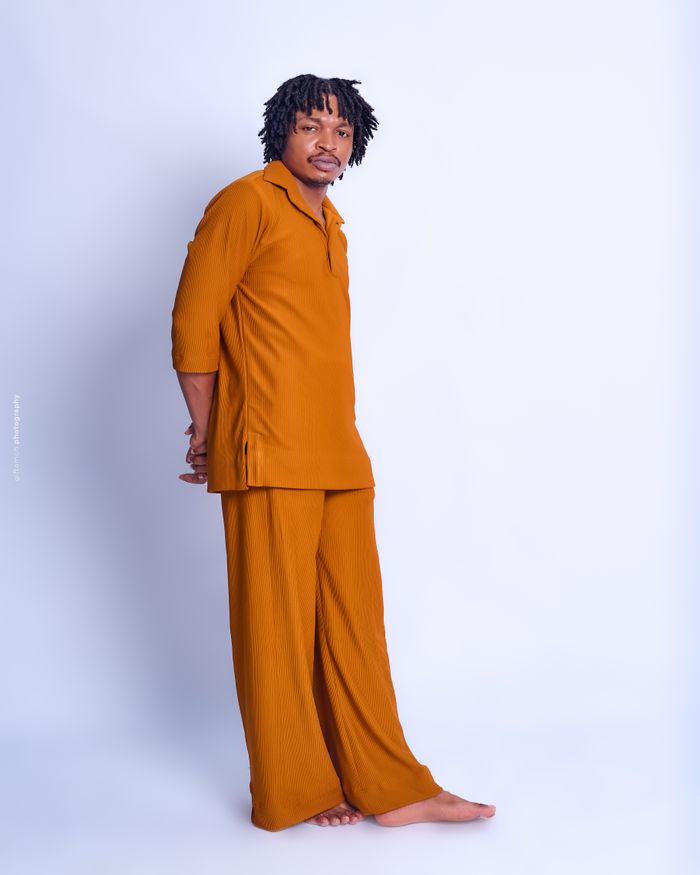 gallery-05 Man in orange outfit posing confidently against a white backdrop, showcasing casual fashion.